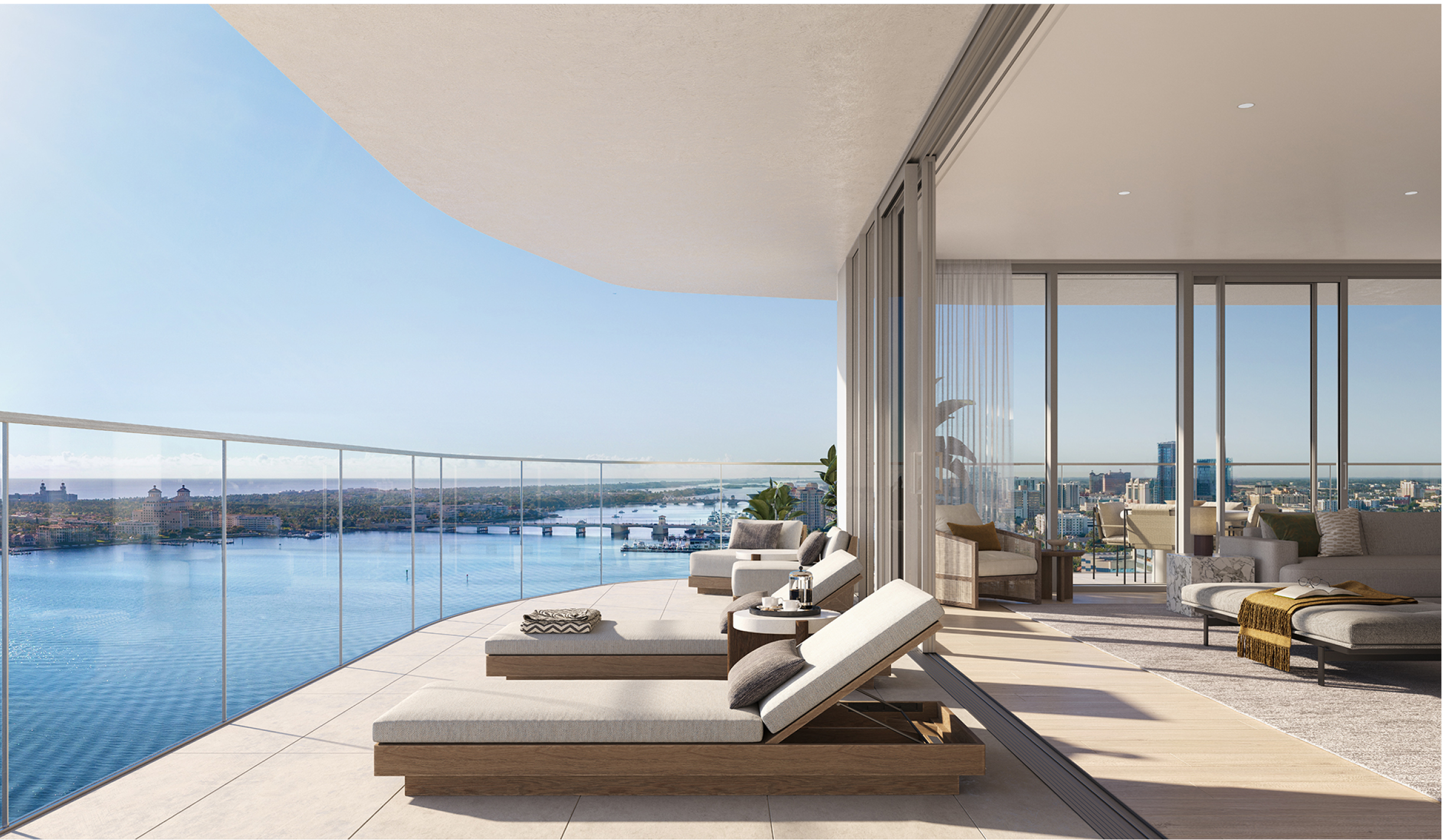 Luxury waterfront condo balcony with cushioned loungers overlooking the ocean and skyline through floor-to-ceiling glass doors.